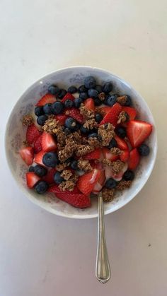 a bowl filled with granola, strawberries and blueberries next to a spoon