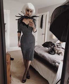 a woman with white hair wearing a black and white striped dress standing in front of a bed