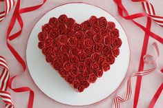 a heart shaped cake on a plate surrounded by red ribbon and streamers, with ribbons in the background