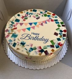 a birthday cake with white frosting and multicolored flags on it sitting in a box