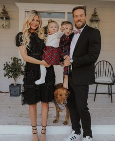 a man, woman and two children standing in front of a house with a dog