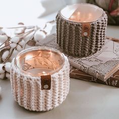 two knitted candle holders sitting on top of a table next to some cotton balls