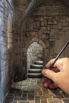 a hand is holding a pen in front of a stone tunnel that has stairs leading up to it