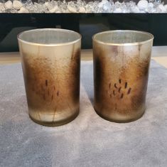 two glasses sitting on top of a table next to each other with brown and black spots