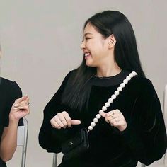 two women sitting next to each other in front of a white wall and one holding a pearl necklace