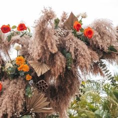 an arrangement of flowers and feathers hanging from a tree in a park or tropical setting