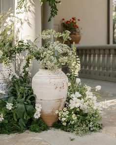 a large white vase sitting on top of a stone floor next to flowers and greenery