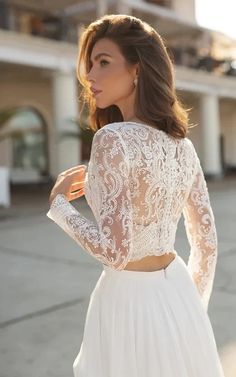 a woman wearing a white wedding dress with long sleeves and lace detailing on the back