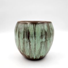 a green and brown vase sitting on top of a white table