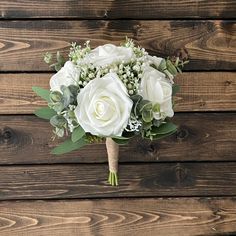 a bridal bouquet with white flowers and greenery on a wooden background, ready to be used as a bride's bouquet