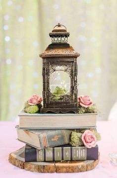 there is a small clock on top of two books and flowers in front of it