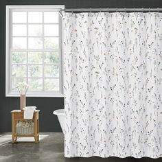 a white shower curtain in a bathroom next to a bathtub and window with flowers on it