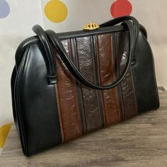 1950's Faux Leather Satchel  Black with Brown Accents  Gold Top Clasp  Excellent Nearly Mint Condition  Interior has a Zippered Pocket and Large Roomy Compartment  Measures: 13" x 8.5" x 5" Strap Drop: 6" Retro Black Bags For Vintage Events, Black Retro Handheld Satchel, Retro Brown Satchel With Top Carry Handle, Black Vintage Bags For Vintage Events, Retro Top Handle Satchel In Vintage Brown, Vintage Black Bag For Vintage Events, Mid-century Style Black Bags, Retro Vintage Brown Bag With Detachable Handle, Mid-century Black Bags For Vintage Style