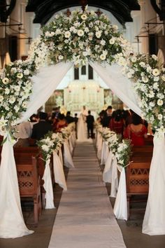 an aisle decorated with white flowers and greenery for a wedding ceremony at the church