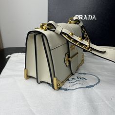 SHOP MORE LUXURY PRODUCTS HERE Description Prada Cahier Bag White For Women, Women’s Bags 7.9in/20cm 1BD045_2AIX_F0009_V_XCH Inspired by the allure of precious and ancient volumes, the Prada Cahier bag is part of Prada’s iconic lines and is presented here in a sophisticated monochrome version with a new color story composed of neutral shades. Featuring antiqued gold-tone hardware that recalls the bindings on books from past eras, the accessory has an adjustable shoulder strap so it c Light Luxury Crossbody Bag With Branded Hardware, Designer Bags With Metal Hardware For Daily Use, High-end Bags With Metal Hardware For Daily Use, Designer Shoulder Bag With Metal Hardware For Daily Use, Designer Shoulder Bag For Daily Use With Metal Hardware, High-end Crossbody Bag With Metal Hardware, Luxury Flap Bag With Branded Hardware For Daily Use, High-end White Bag With Adjustable Strap, High-end Beige Shoulder Bag With Branded Hardware