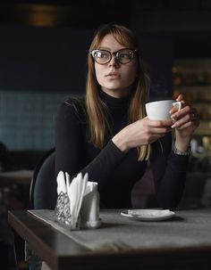 a woman sitting at a table holding a coffee cup