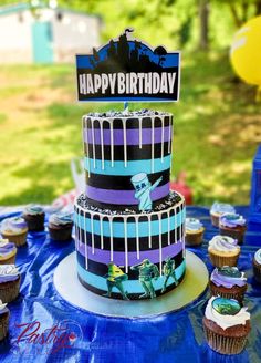 a birthday cake with cupcakes on a table in the grass and trees behind it