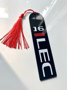 a red tassel hanging from the hood of a white car with black lettering on it