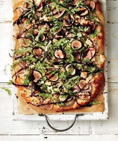 a pizza topped with figs and greens on top of a wooden cutting board