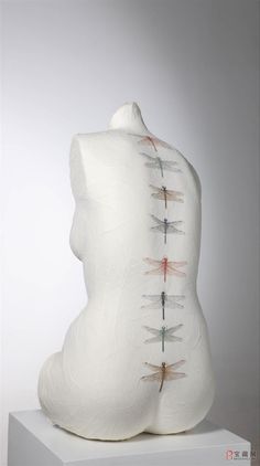 a white sculpture with dragonflies painted on it's back and neck, sitting on a pedestal