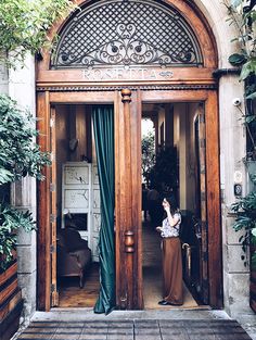 a woman standing in the doorway of a building with green curtains on it's windows