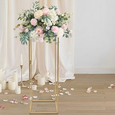 a floral arrangement on a gold stand in front of a white backdrop with candles and flowers