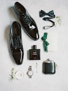 the groom's accessories are laid out neatly on the white surface, including black shoes and watch