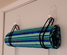 a blue and green striped bag hanging from a hook on a white door with black straps