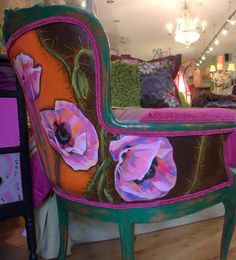 a chair with flowers painted on it in front of a bed and dresser at a store