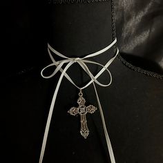 This necklace has a long white ribbon and a metal cross pendant, intended to be wrapped multiple times around the neck. It is about 62 inches long. Elegant Cross Choker As A Gift, Elegant Silver Cross Choker, Vintage White Cross Jewelry, Adjustable Silver Cross Choker, Adjustable White Cross Necklace, Adjustable White Cross Necklaces, Adjustable Silver Cross Lariat Necklace, White Spiritual Crucifix Cross Necklace, White Crucifix Cross Necklace