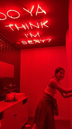 a woman standing in a room with red lights on the ceiling and a neon sign above her