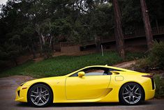 a yellow sports car is parked in front of a wooded area with trees and bushes