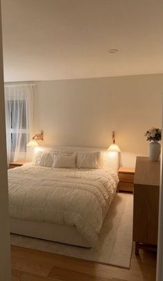 a large white bed sitting inside of a bedroom next to a wooden dresser and window