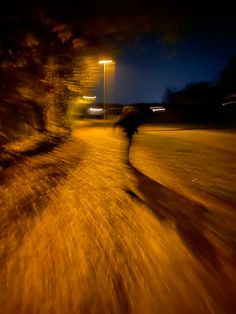 a blurry photo of a person walking down a road at night with street lights in the background