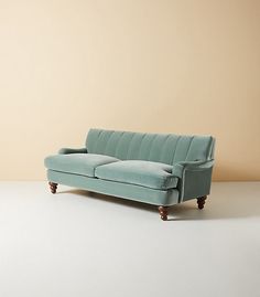 a blue couch sitting on top of a white floor next to a beige wall and wooden legs