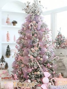 a pink christmas tree decorated with ornaments and bows