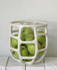 a white bowl filled with green apples sitting on top of a brick counter next to a wall