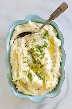 mashed potatoes in a blue bowl with a spoon on the side and parsley sprinkled on top