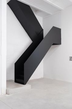 an abstract black sculpture in the middle of a white room with stairs leading up to it