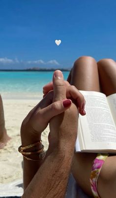 a person sitting on the beach reading a book with a white heart floating above them