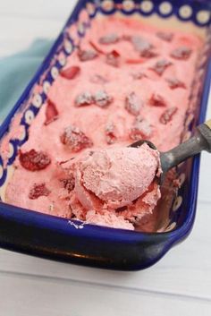 a scoop of strawberry ice cream in a blue dish with a spoon on the side