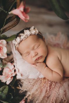 a baby is laying down with flowers in her hair and it's eyes closed