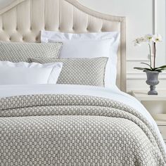 a white bed topped with pillows next to a vase filled with flowers on top of a wooden headboard