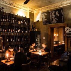 people sitting at tables in a restaurant with wine bottles on the wall