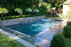 an empty swimming pool in the middle of a yard with trees and bushes around it