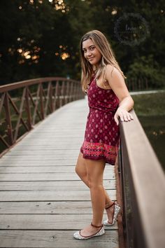 a beautiful young woman standing on a wooden bridge