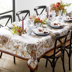 a dining room table set with place settings and flowers on the table cloth, surrounded by black chairs