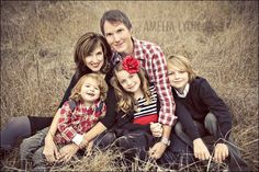 a family is sitting in the tall grass posing for a photo with their two children