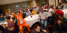 a large group of people sitting at tables in a room with white tablecloths