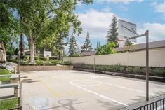 an empty basketball court in the middle of a residential area with lots of trees and bushes